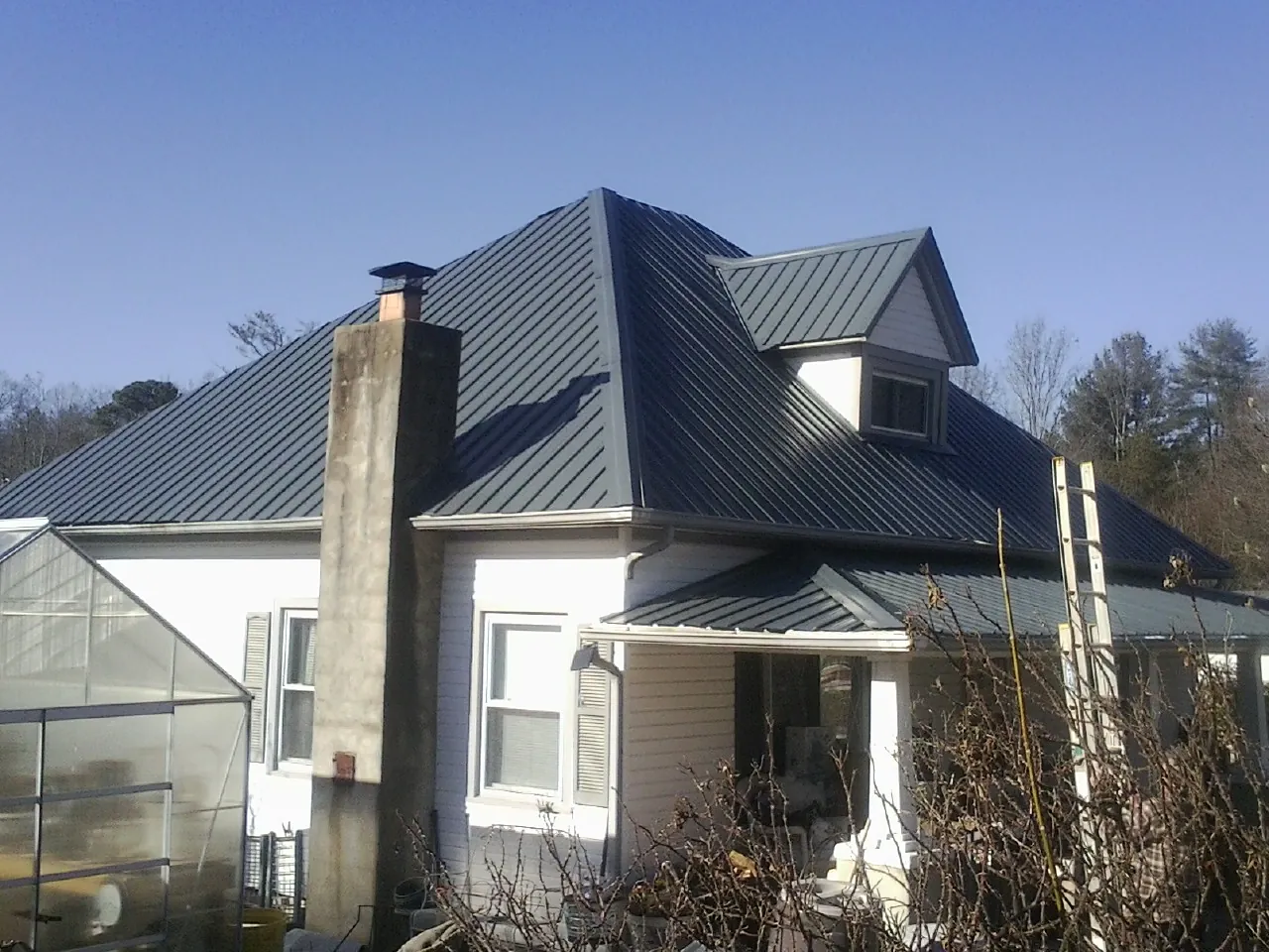 Dark blue standing seam metal roof on a white farmhouse with dormer — Slate & Tile Roof Repair by Roofing Brothers in Pawnee