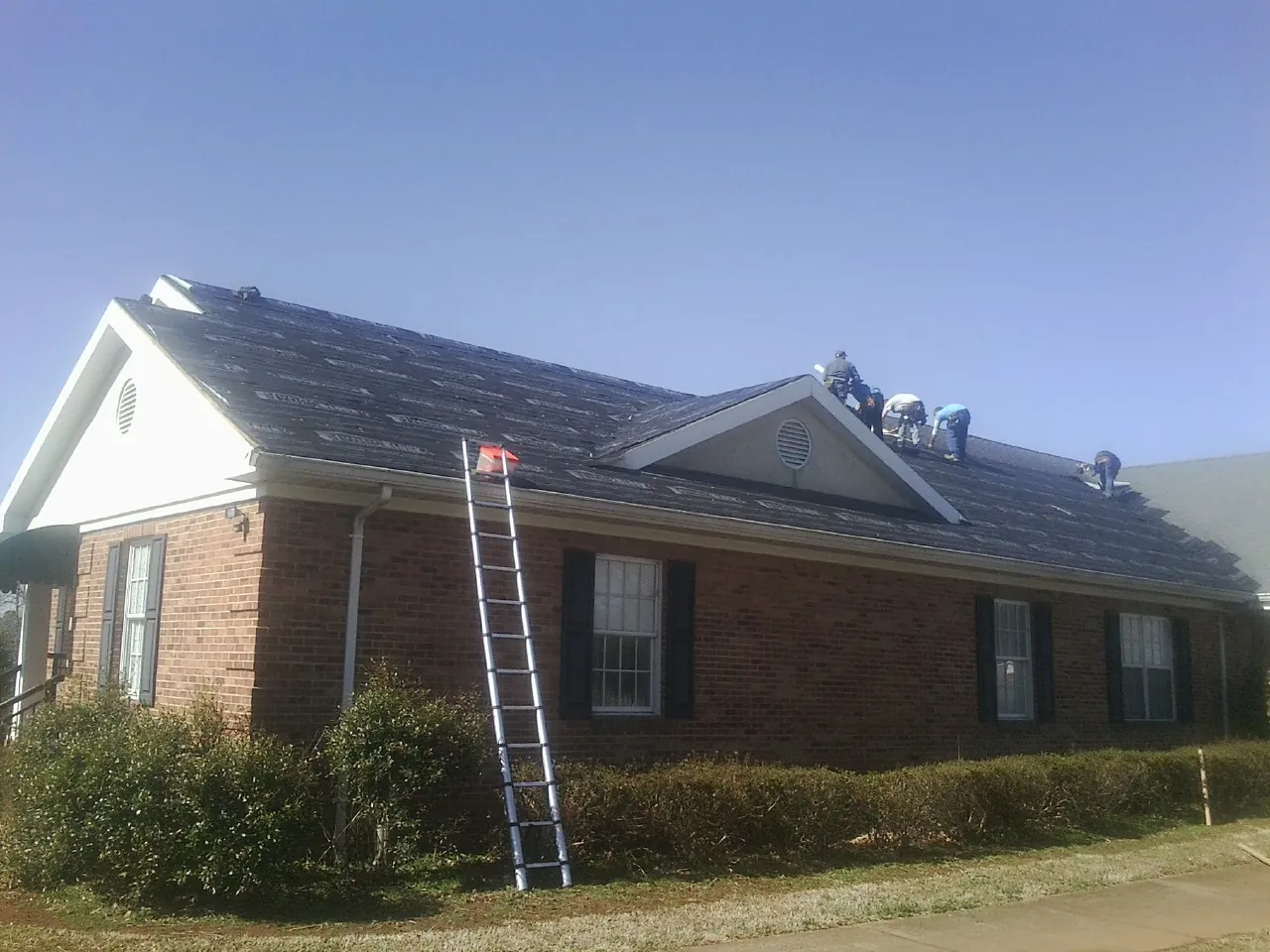 Crew tearing shingles off a brick ranch roof with a ladder set — Metal Roof Repair work by our crew in Pawnee