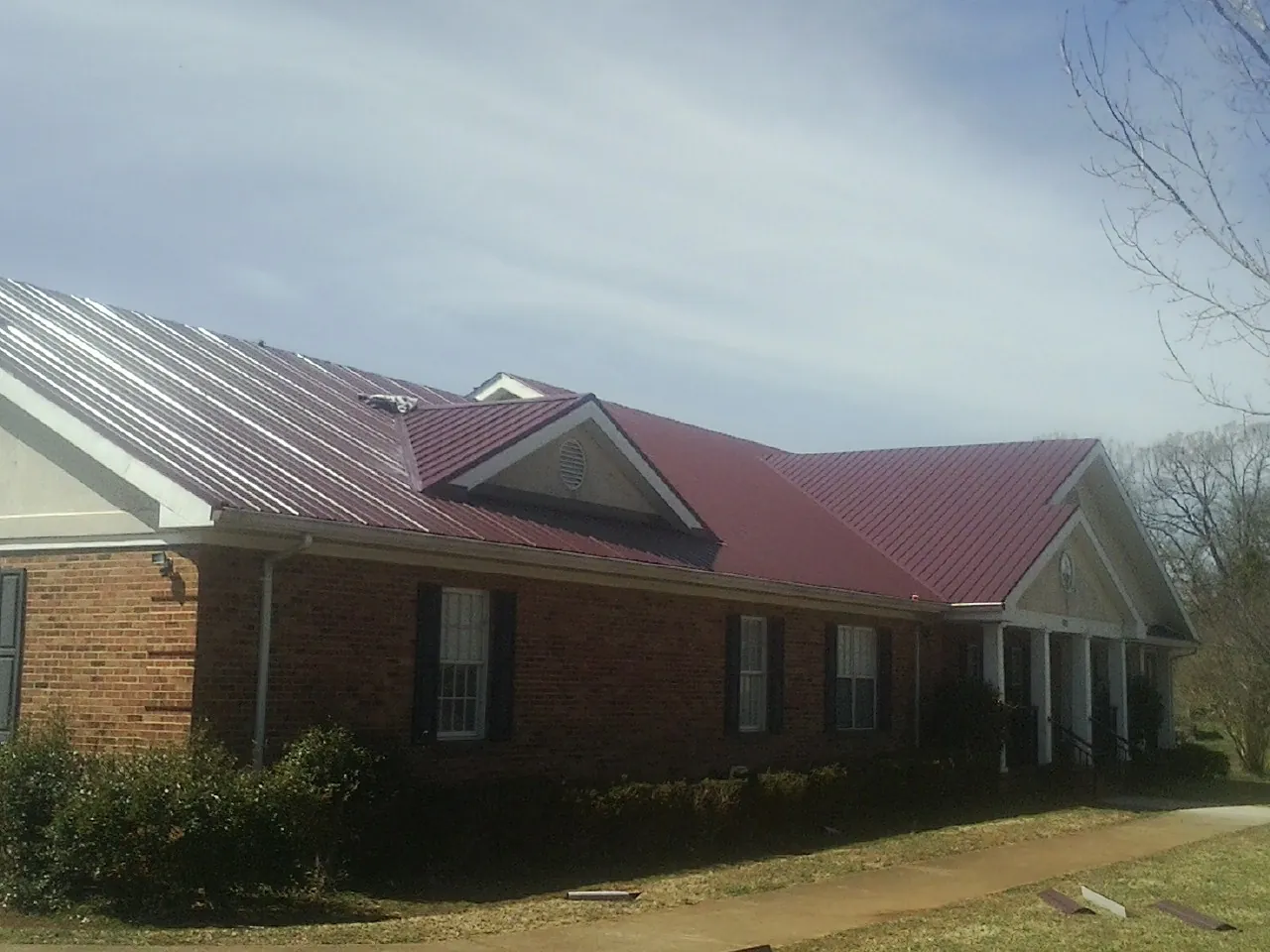 Red metal roof with gabled entries on a long brick building, from a Hail Damage Roof Repair job in Pawnee