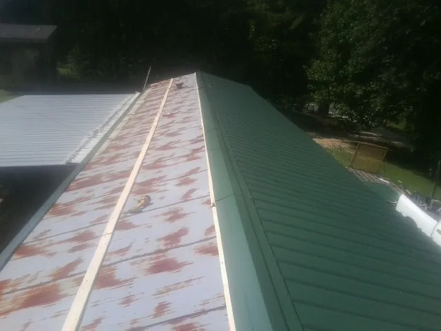 Old rusted panels beside newly installed green metal roofing — Wind Damage Roof Repair by Roofing Brothers in Pawnee