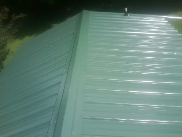 New green metal panels meeting at the ridge of a roof — Flat Roof Repair work by our crew in Pawnee