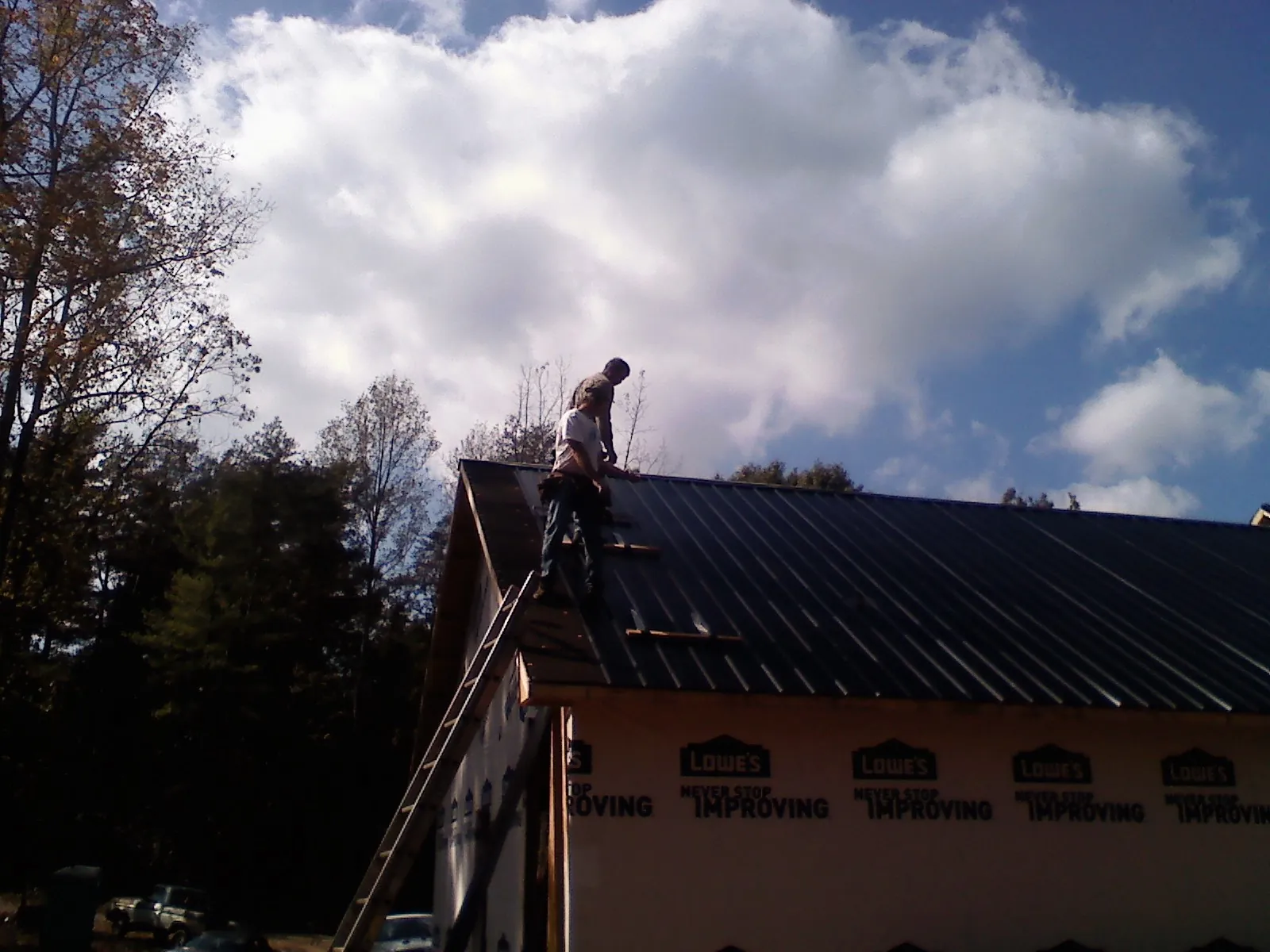 Roofer fastening dark metal panels high against a cloudy sky, from a Roof Inspection job in Pawnee