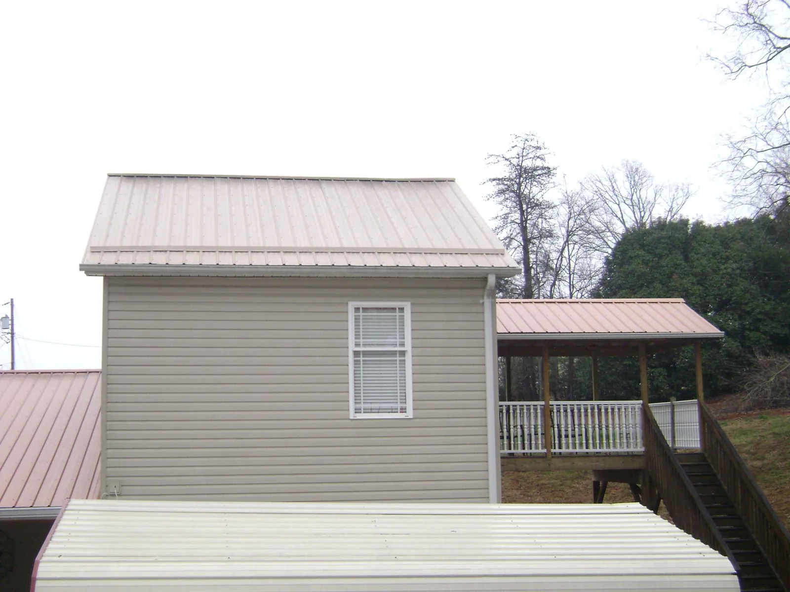 Tan metal roofs on a two story addition and attached porch, from a Roof Replacement job in Pawnee